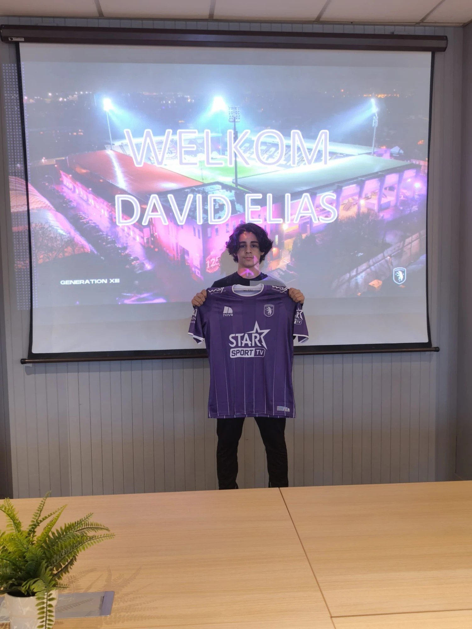 David Elias présente le maillot violet du K. Beerschot V.A. devant un écran « Welkom David Elias »